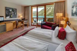 Tweepersoonskamer Een kamer met twee bedden, een tafel en stoelen, uitzicht op een meer.