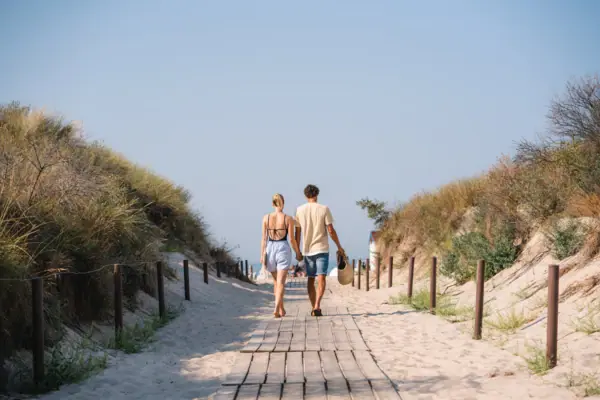 Een vrouw en een man lopen hand in hand naar de strandopgang in Warnemünde.