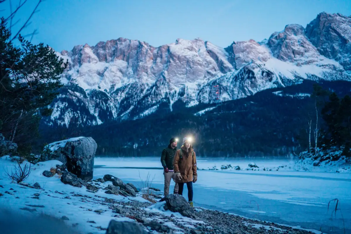 Winterwandeling Een koppel staat met koplampen op een rotsachtige oever.