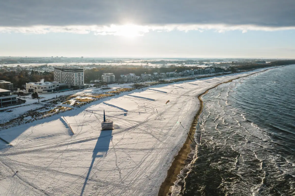 Winter in Warnemünde Een met sneeuw bedekt strand met gebouwen en water in de winter.