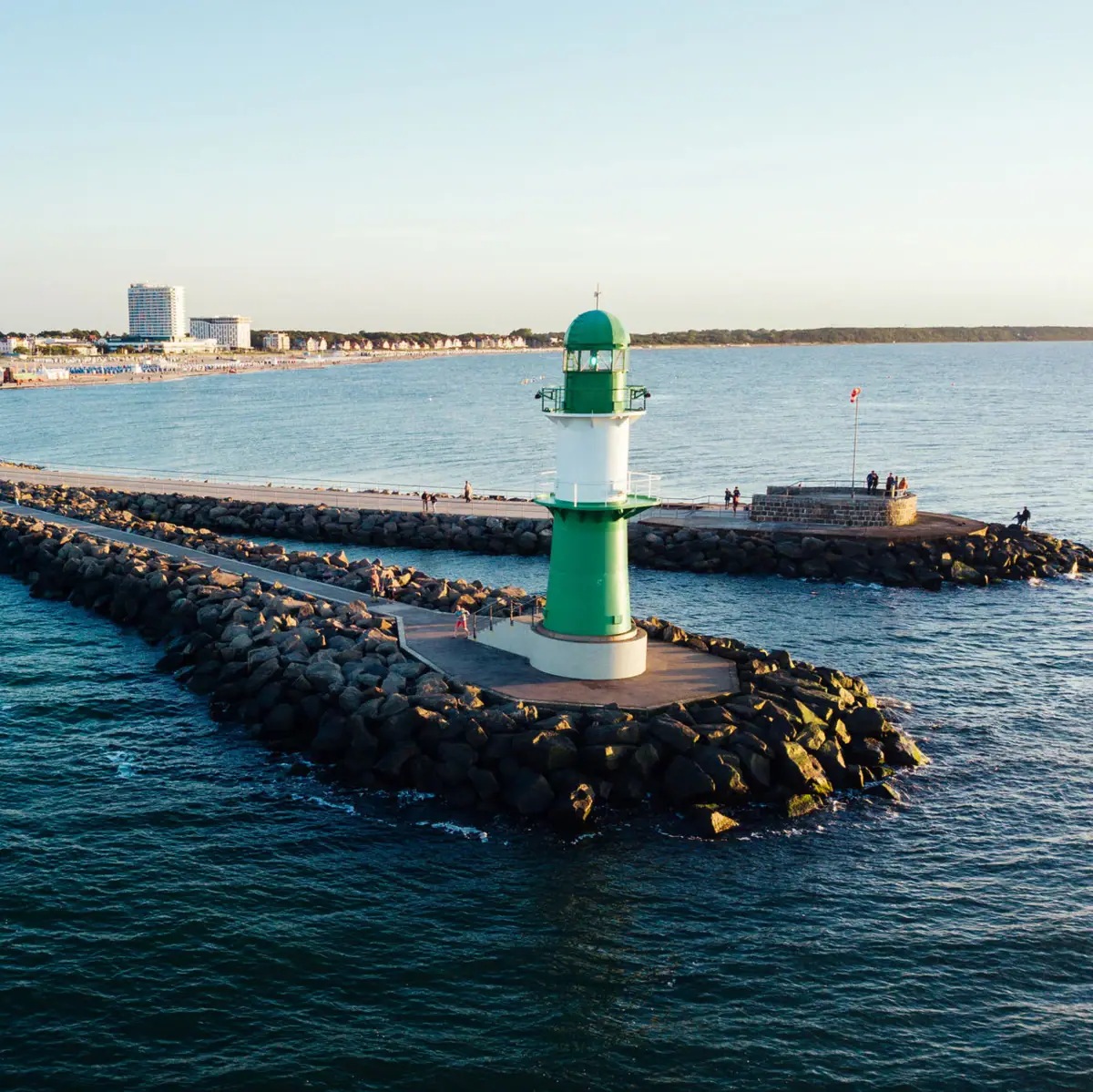 Warnemünde Een groene en witte vuurtoren op rotsen in het water.