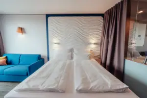 Een bed met witte lakens en een blauwe bank.