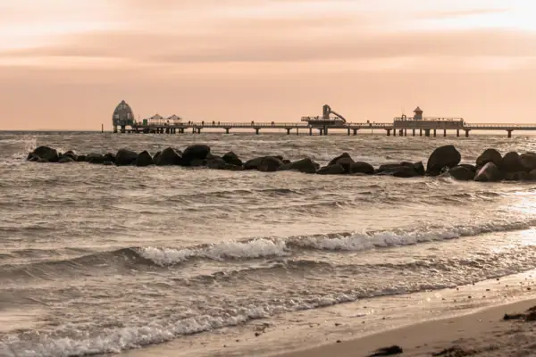 Strand met een pier en rotsen bij zonsondergang.