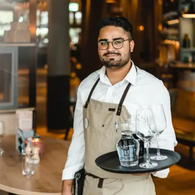 Servicemedewerkers Een man houdt een dienblad met wijnglazen en een fles vast.