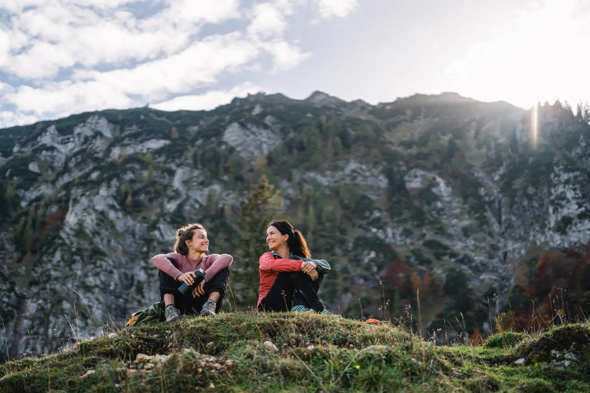 Wandelen in Ruhpolding Twee vrouwen zitten op een heuvel met bergen op de achtergrond.