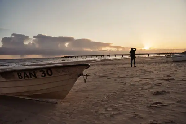 Een persoon staat op het strand naast een boot.