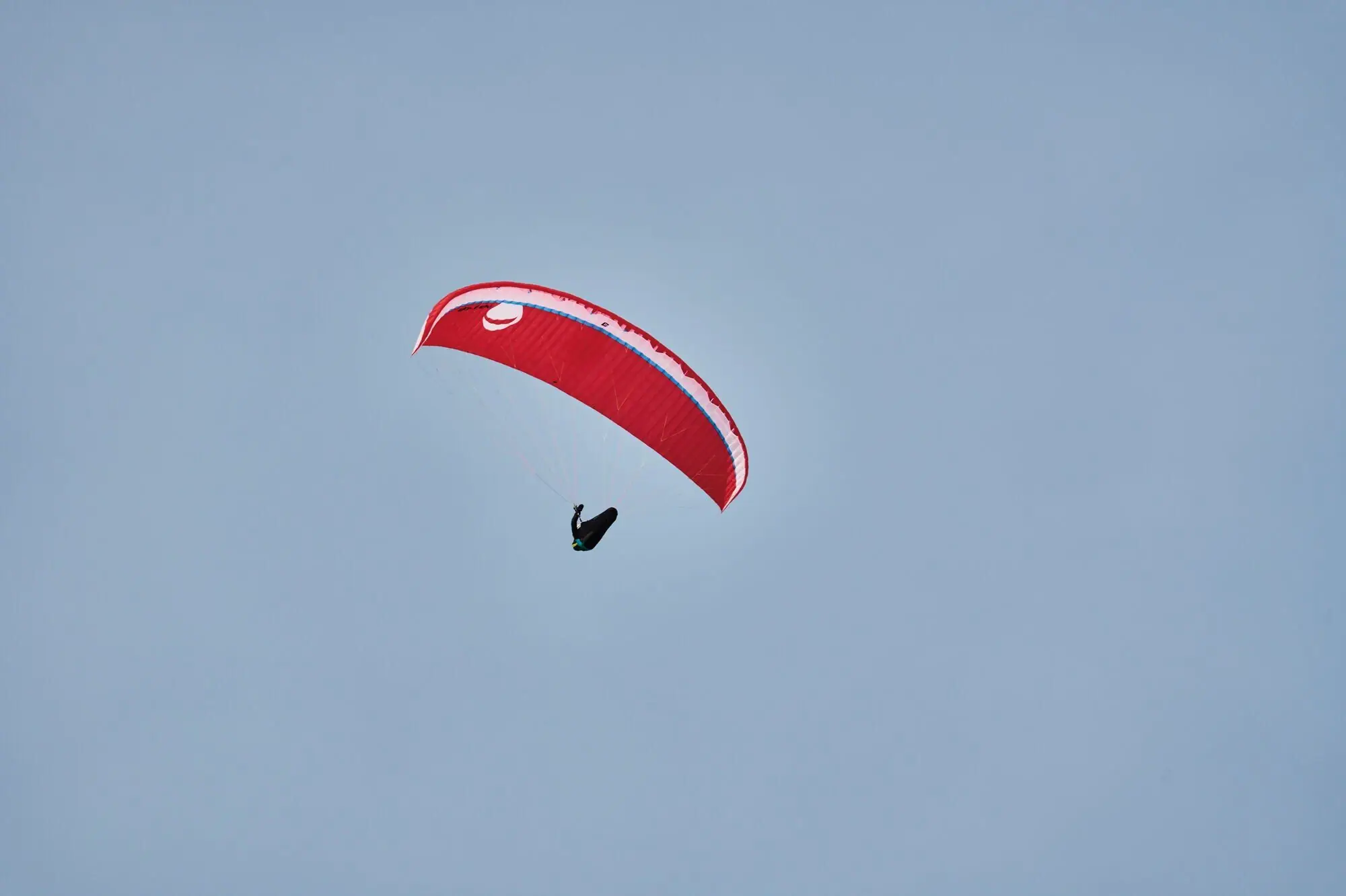 Een persoon die paragliding doet met een rood paraglider zweeft voor de blauwe lucht.