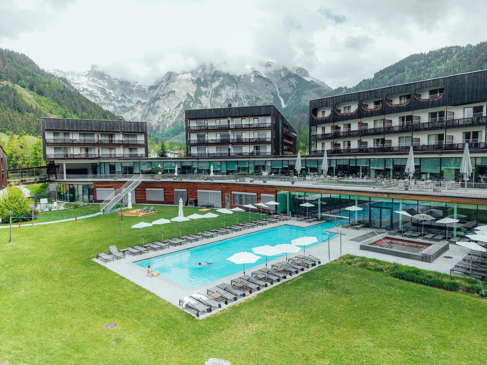 Een buitenzwembad bij een hotel, met een grasveld en bergen op de achtergrond.