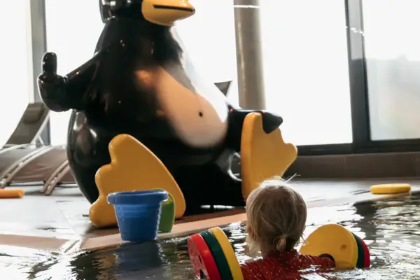 Een kind zwemt in een zwembad naast een pinguïnbeeld.