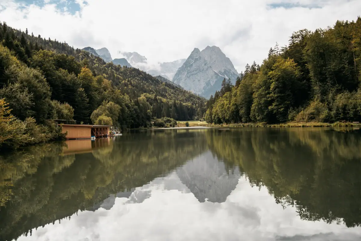 Riessersee Een meer met een huisje en bergen op de achtergrond.