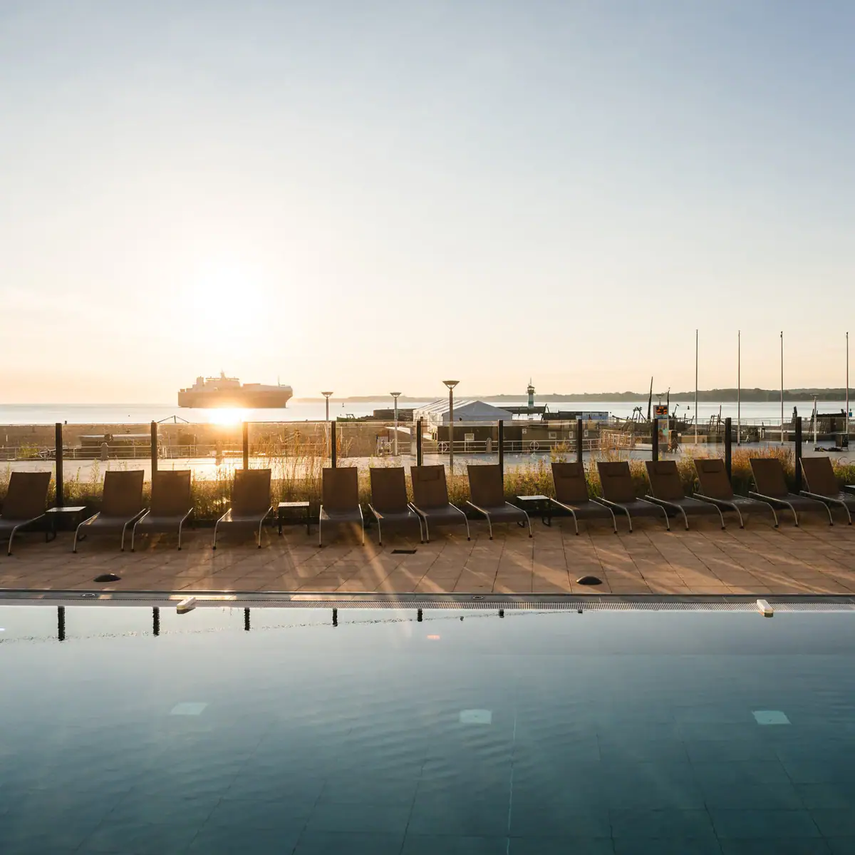 Een zwembad met stoelen en een boot op de achtergrond.