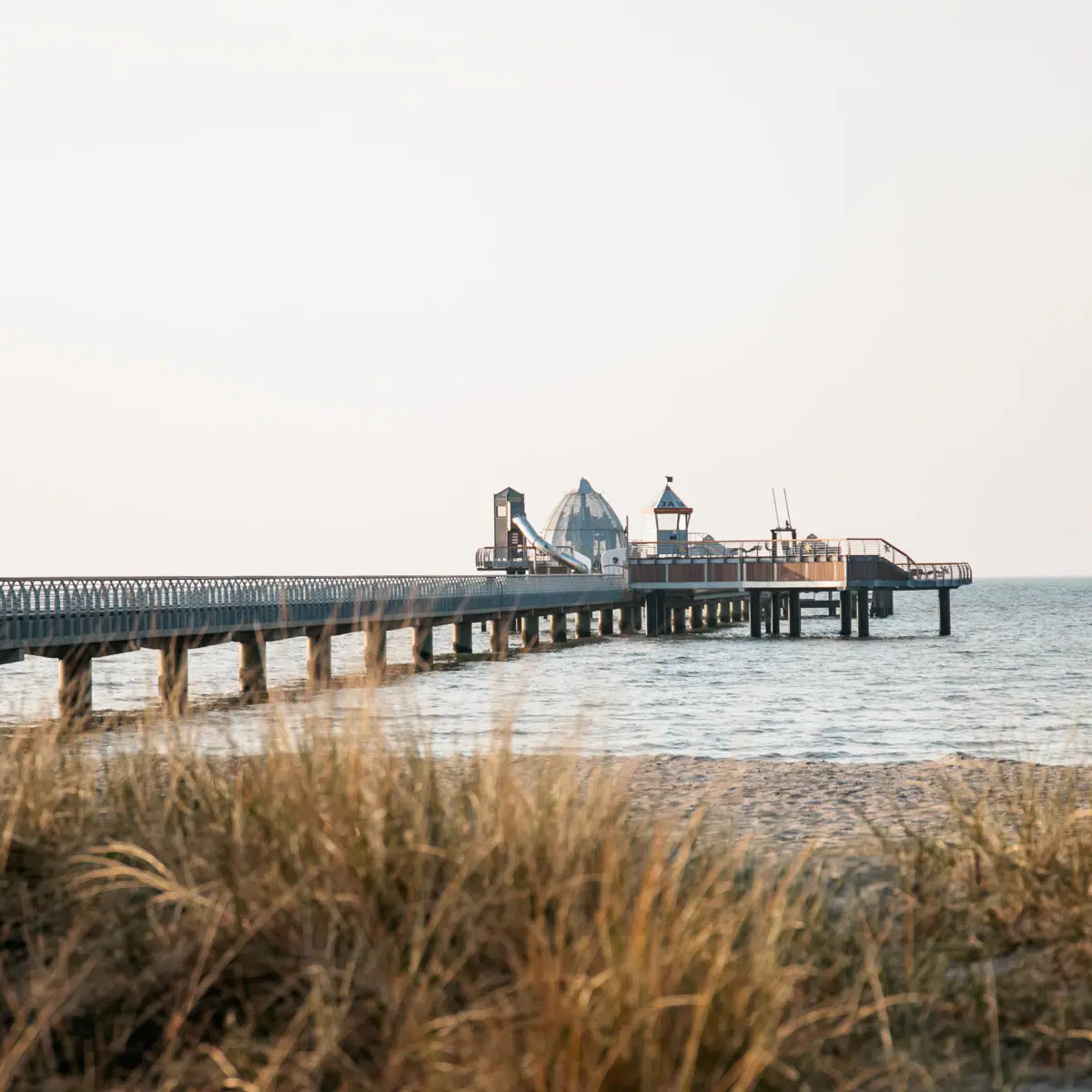 Lange pier aan het strand met gras op de voorgrond.