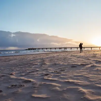 Een persoon loopt langs het strand onder een bewolkte hemel.