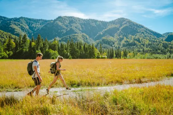 Wandelen in Ruhpolding Een man en een vrouw lopen in een veld met bergen op de achtergrond.
