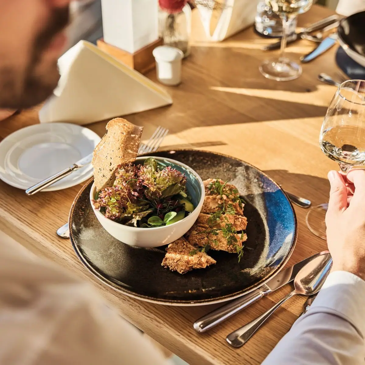 Restaurant Feinspitz Man eet salade en drinkt een glas wijn aan tafel.