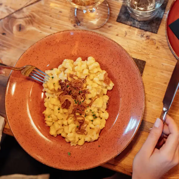 Een bord met macaroni met kaas, met daarnaast een vork en een mes.