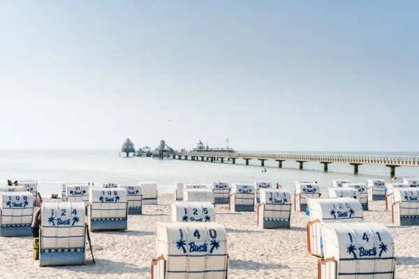 Strand met witte strandstoelen en blauwe strepen tegen een heldere hemel.