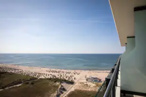 Suite bij de aja Warnemünde Uitzicht vanaf het balkon. Strand met mensen, lucht en wolken op de achtergrond.