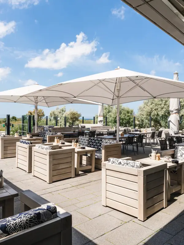 Die Terrasse von der The View Bar & Lounge, der aja Strandbar Warnemünde, mit Tischen und Stühlen.
