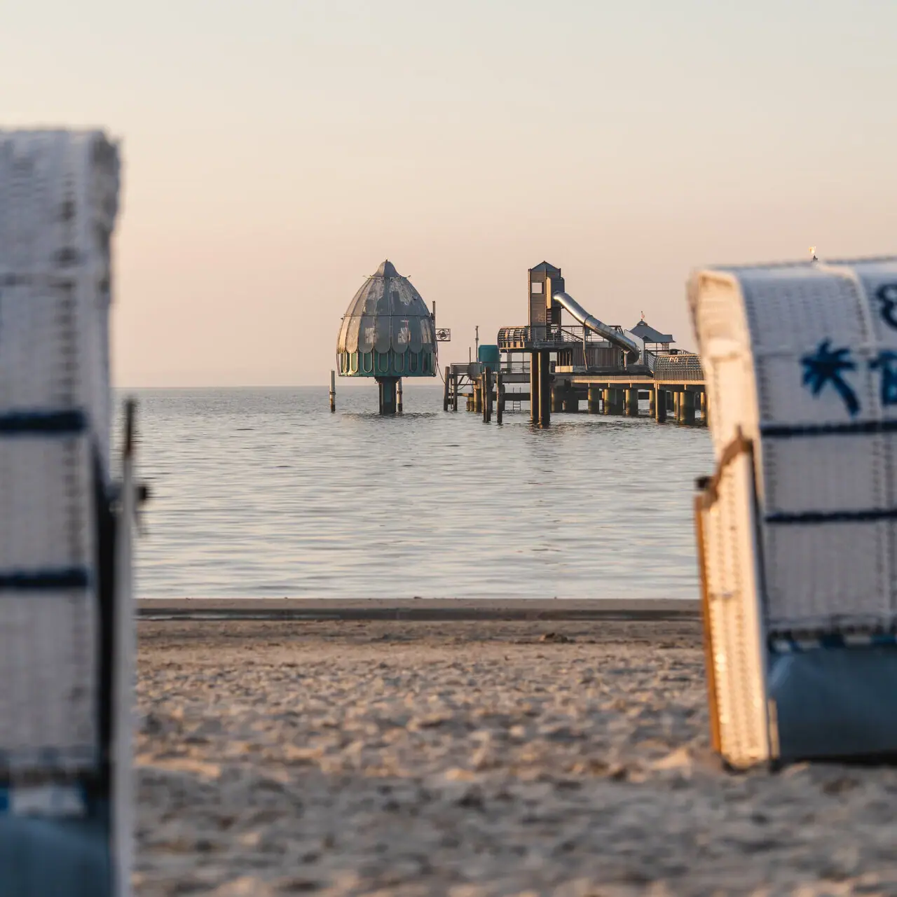 Strandstoelen op het strand met uitzicht op het water en de duikgondel van Grömitz.