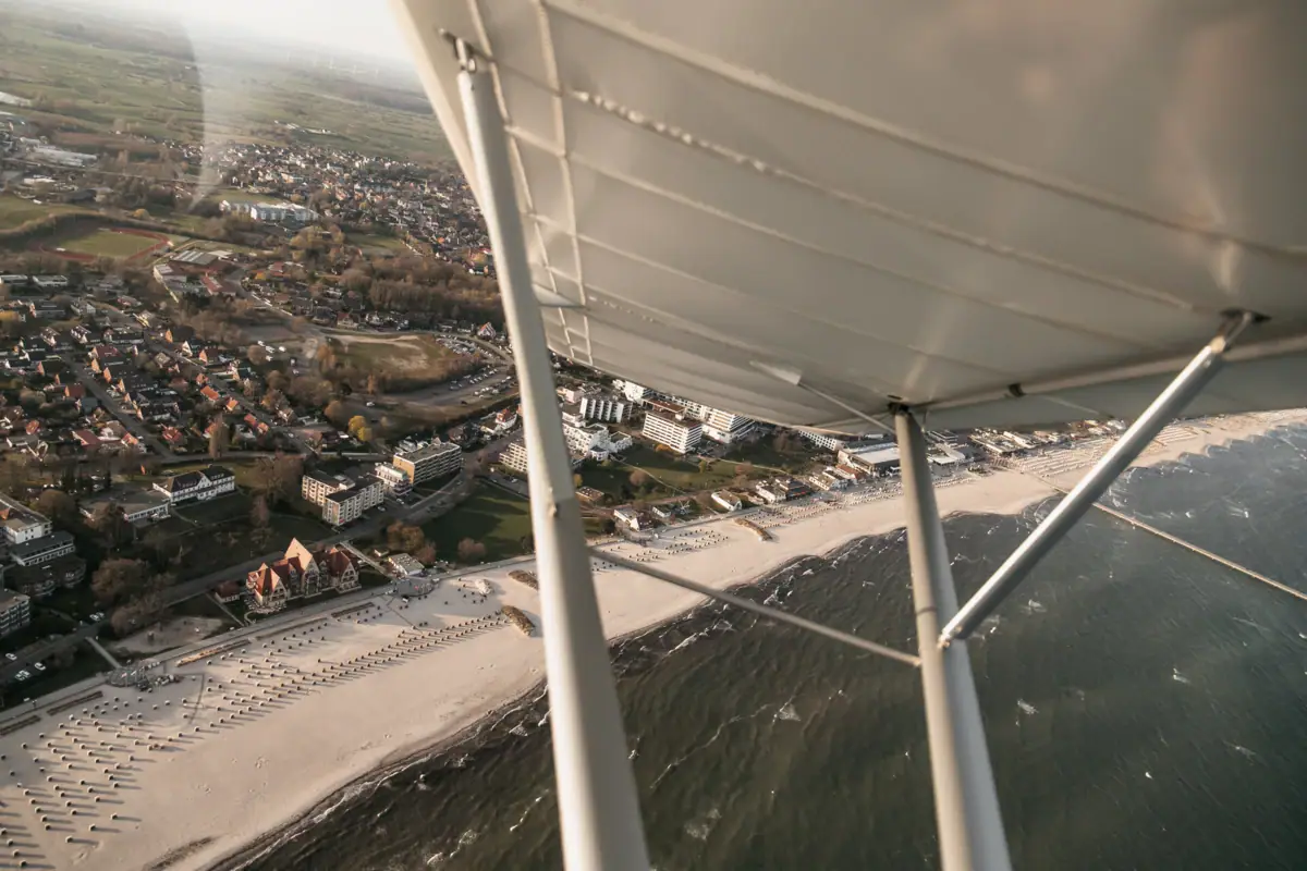 Een vliegtuigvleugel boven een strand, met gebouwen op de achtergrond.