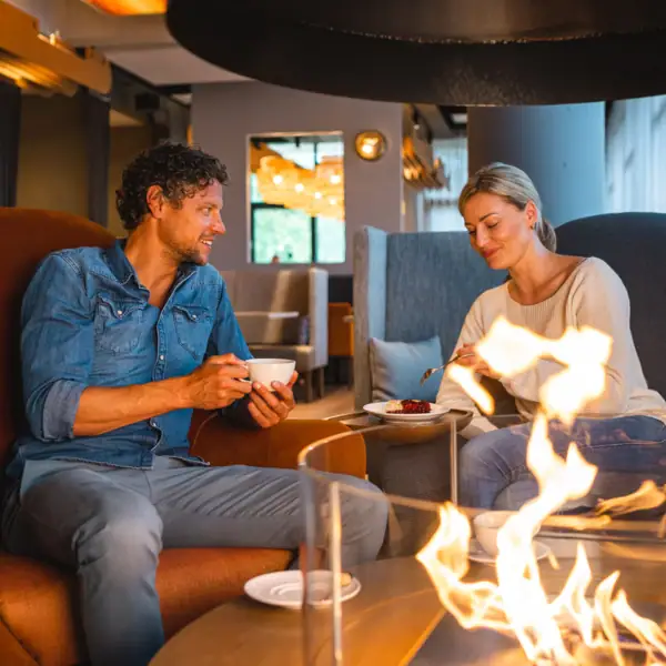 Restaurant en bar bij aja Warnemünde Een man en een vrouw zitten op een stoel en eten bij een open haard.