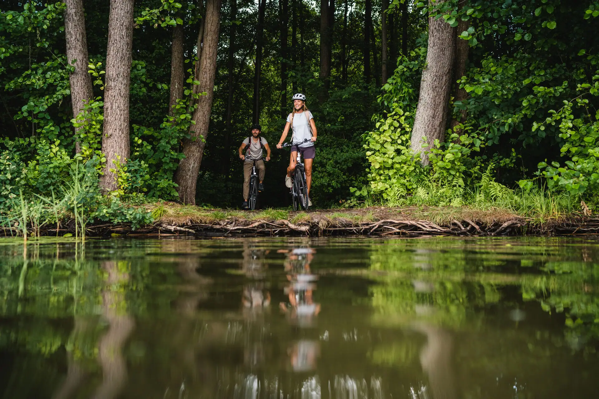 Een man en een vrouw op de fiets aan de oever van een waterlichaam.