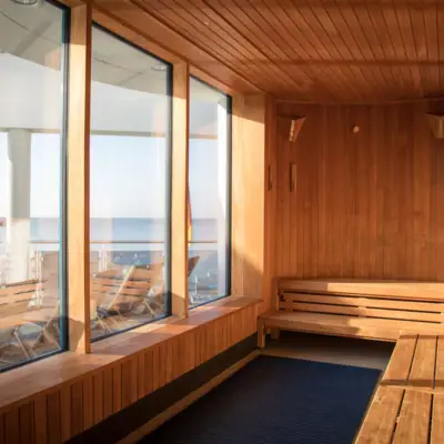 Uitzicht vanuit een houten sauna door drie brede panoramische ramen op het zandstrand en het water van de Baltische Zee.
