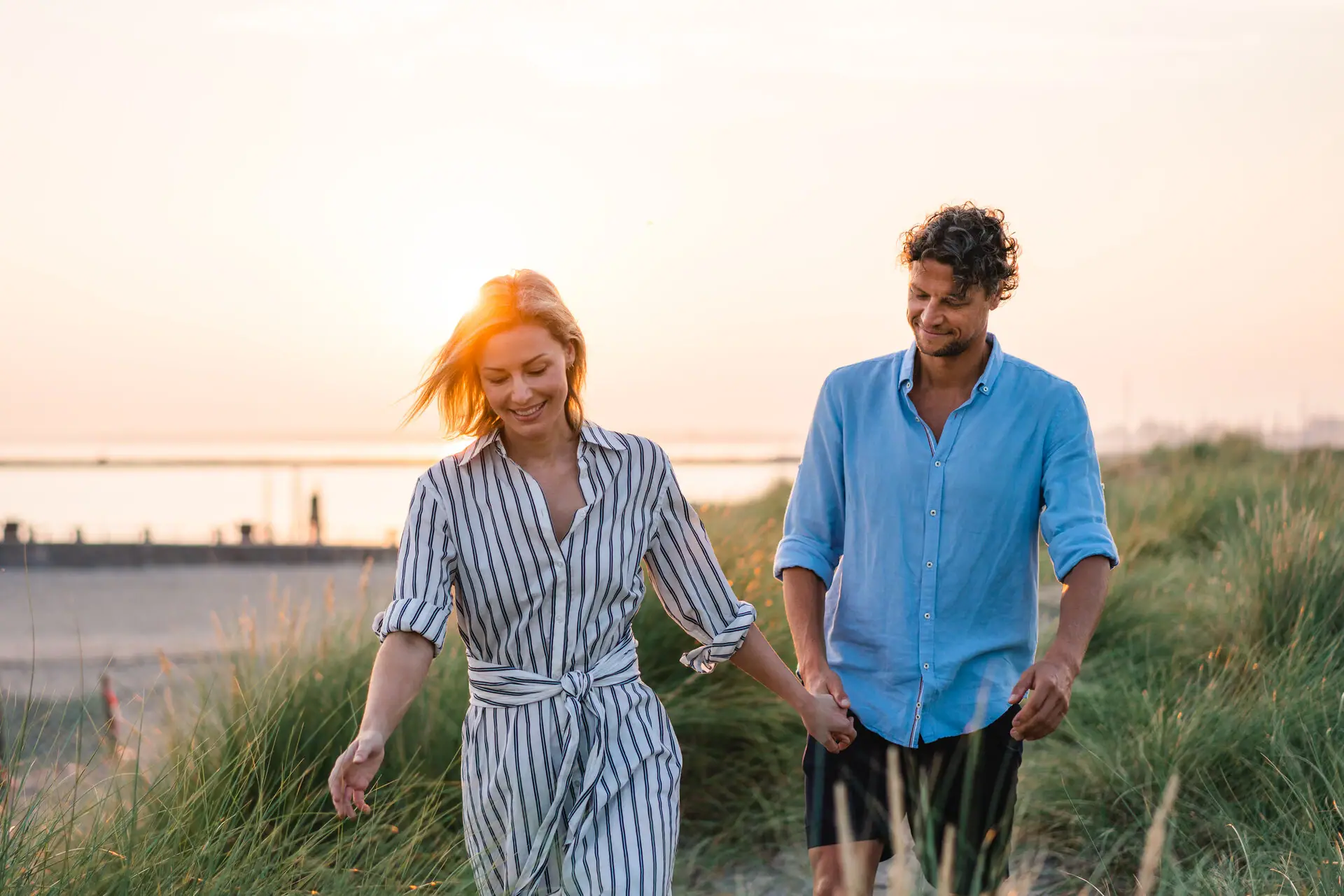 Een man en een vrouw houden elkaars hand vast en lopen in een grasveld.