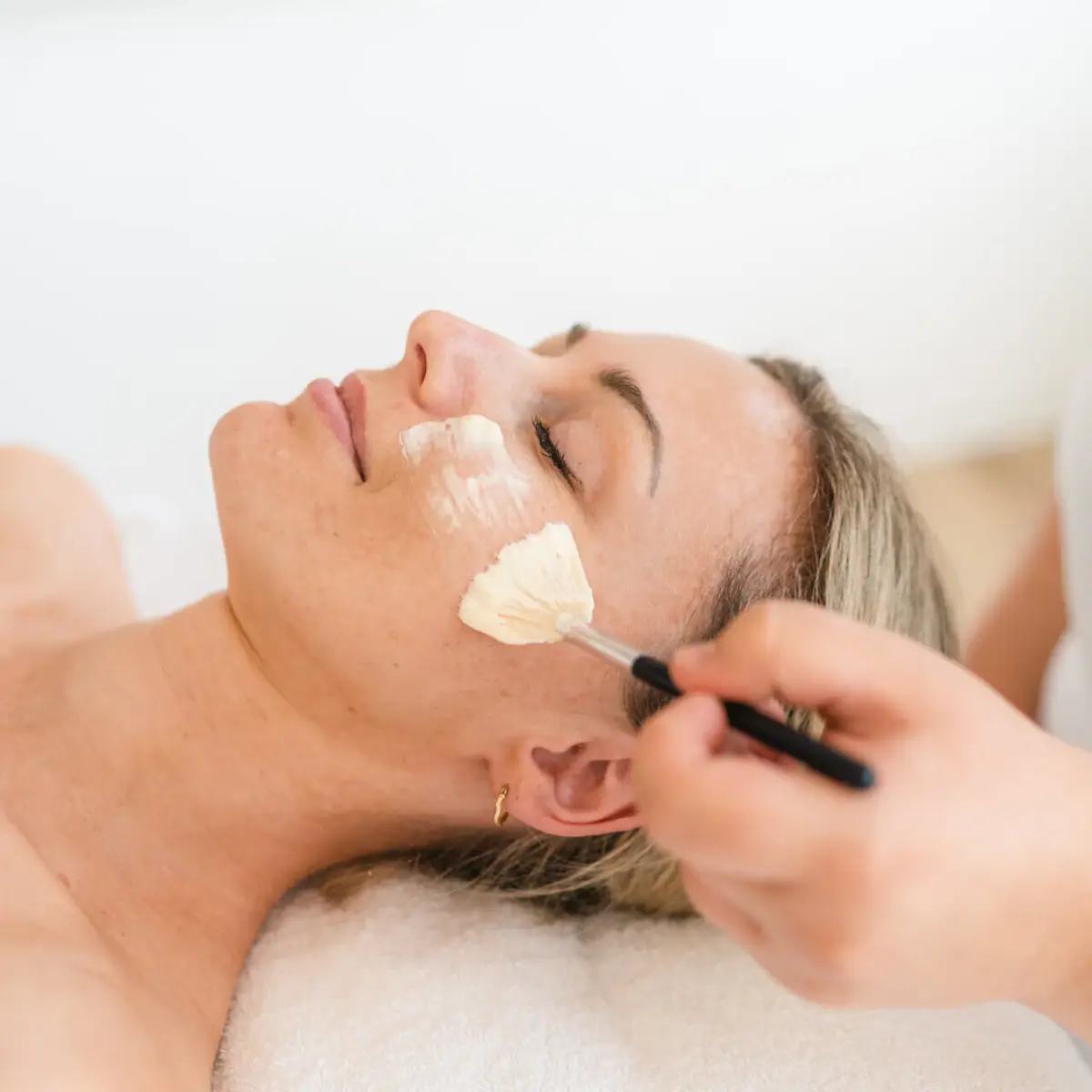 Toepassing op het gezicht Een vrouw ligt ontspannen terwijl er een borstel over haar gezicht wordt gehaald.