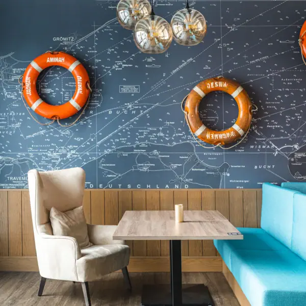 JEDERMANNS Restaurant Grömitz Een tafel en stoelen, met een blauwe bank en oranje reddingsboeien aan de muur.