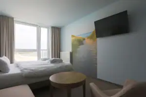 Tweepersoonskamer  Een kamer met een bed, een tafel en een televisie.