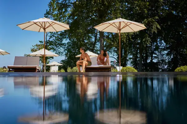 SPA Ein Mann und eine Frau sitzen am Poolrand mit Sonnenschirmen.