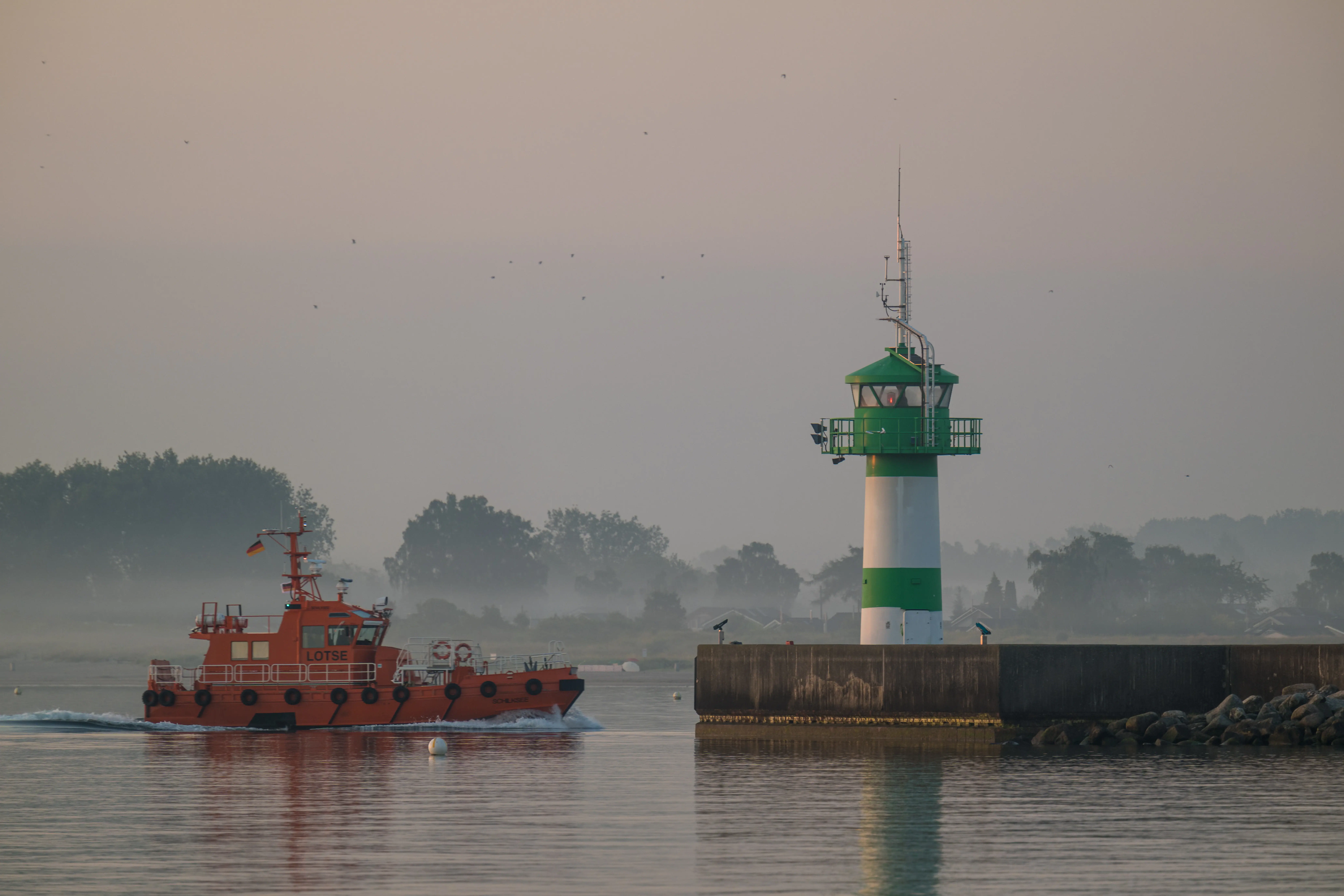 Een boot op het water met een vuurtoren op de achtergrond.