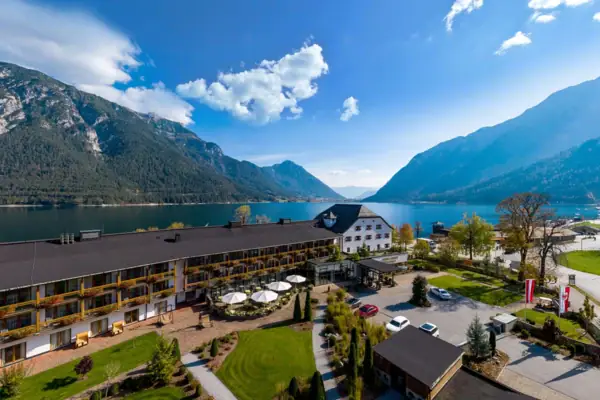 Een gebouw bij een meer met wolken in de lucht en bomen op de voorgrond.