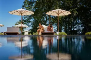 Ein Mann und eine Frau sitzen am Poolrand mit Sonnenschirmen.