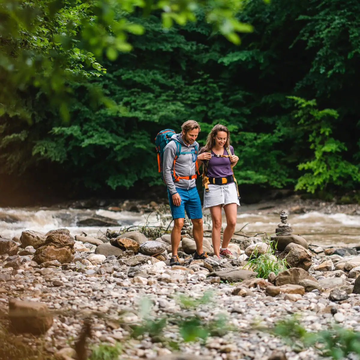 Wandelen in de rivierbedding Een man en een vrouw staan op rotsen bij een rivier.