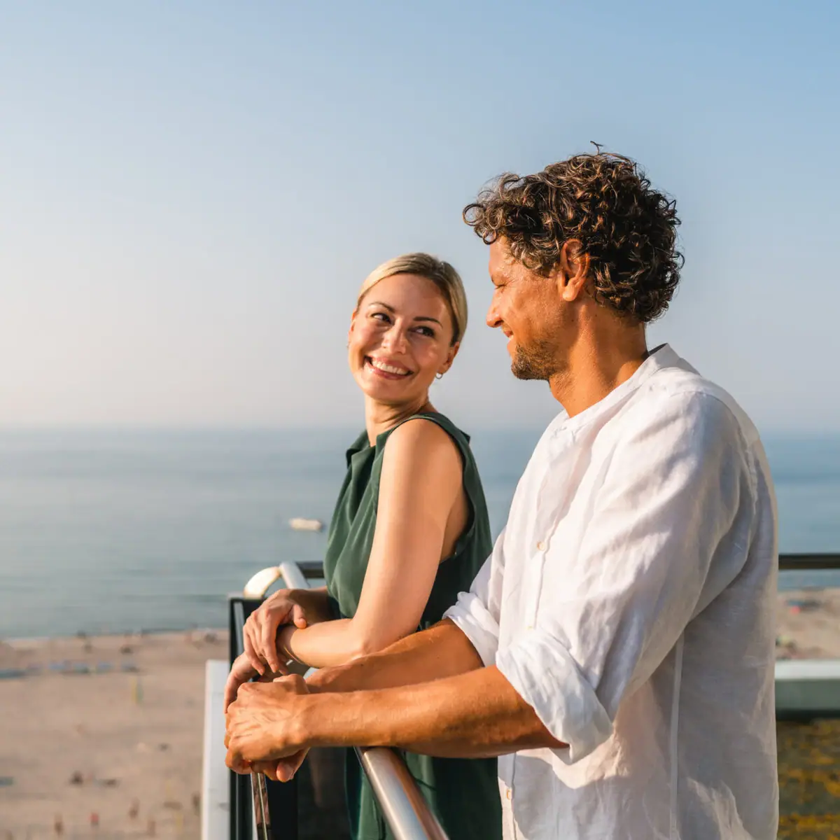 Een man en een vrouw staan op een balkon met uitzicht op een strand.