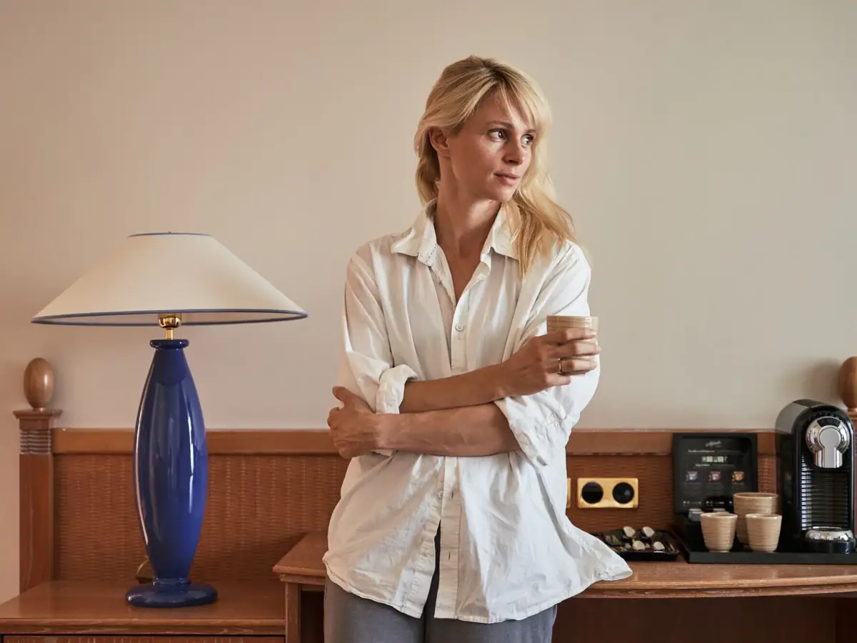 Kamer Een vrouw staat voor een tafel met een lamp en een koffiekopje.