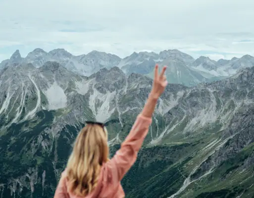 Actief met aja  Een vrouw staat op een berg en steekt haar hand op.