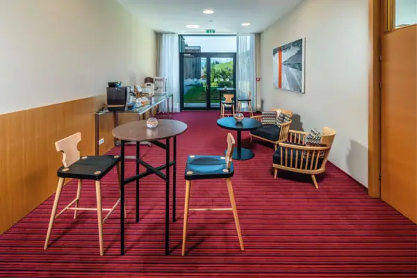 Een ruimte met een rode loper, verspreide zitplaatsen, een koffiebar en een grote patiodeur aan de achterkant. 