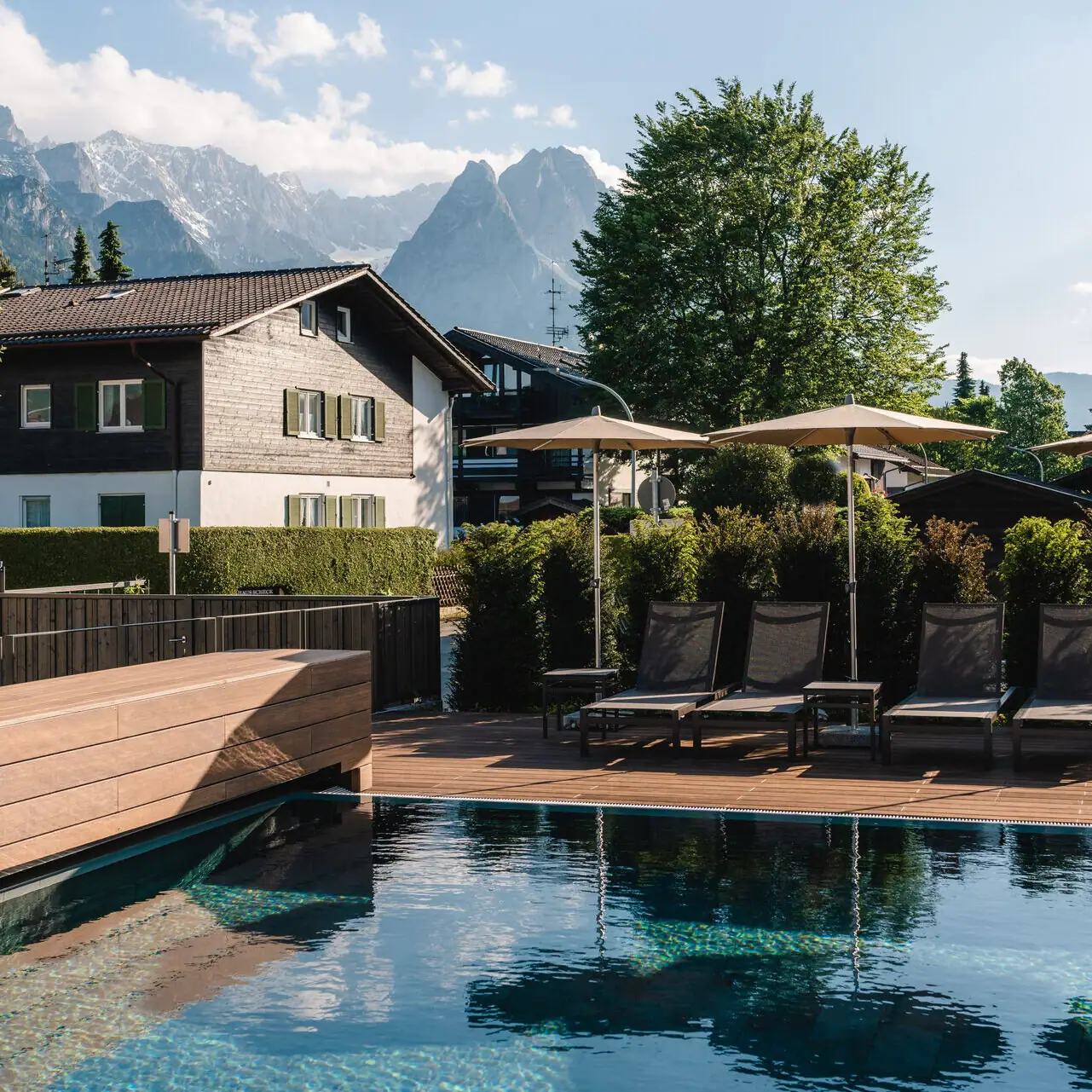 Buitenzwembad aja Garmisch-Partenkirchen Een zwembad met stoelen en parasols naast een huis.