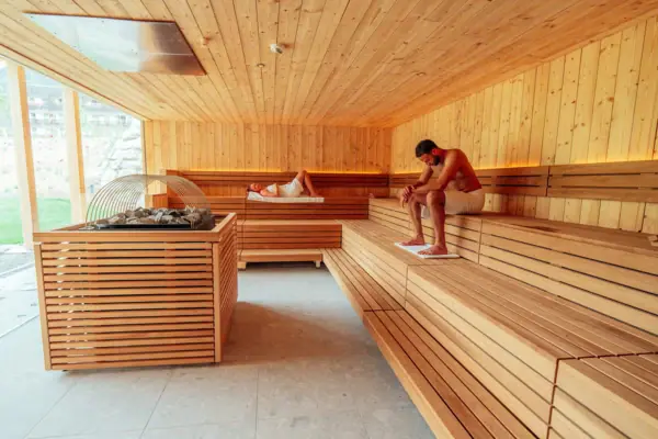 Sauna Een man zit op een bankje in een kamer met houten lambrisering.