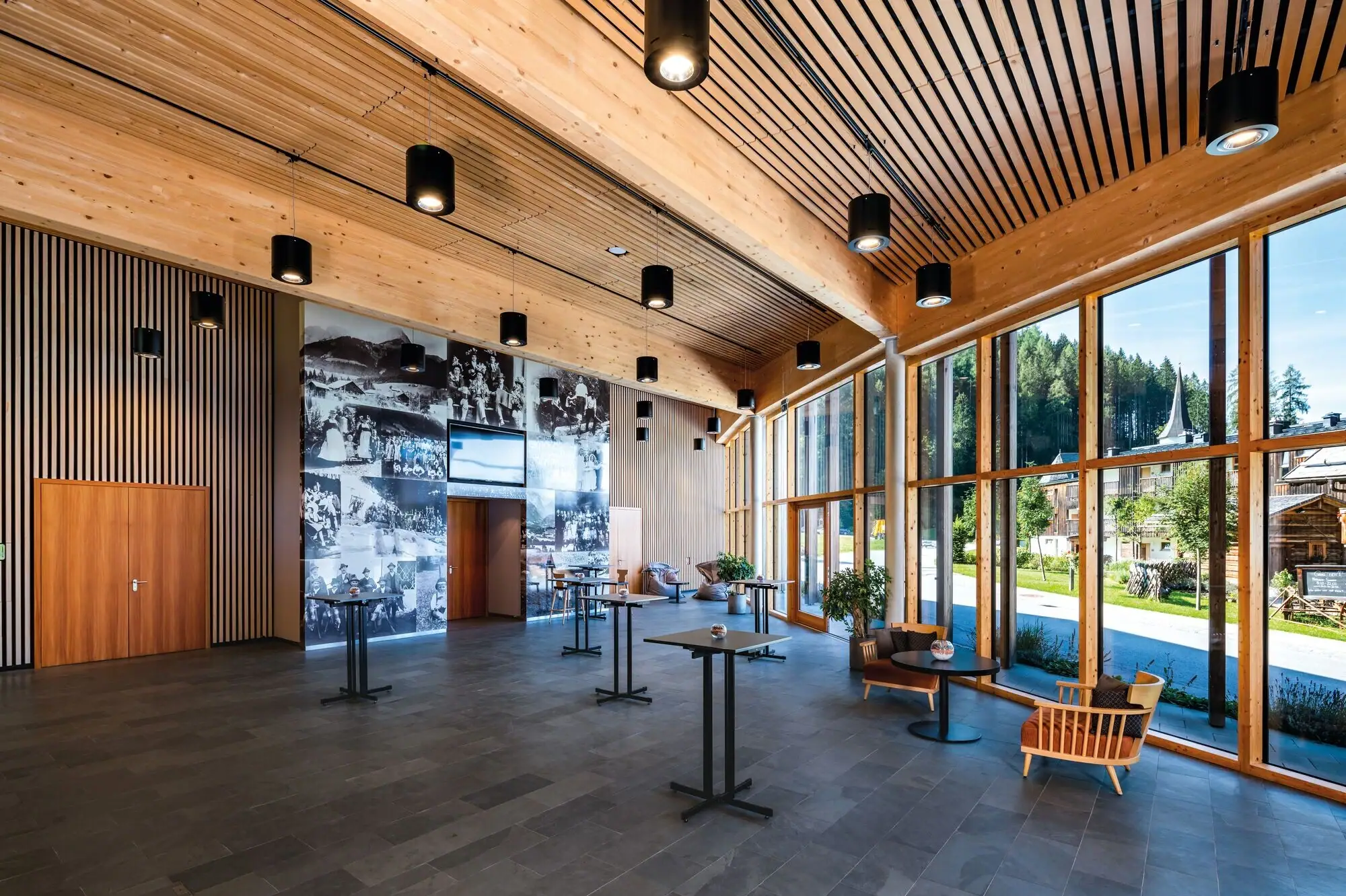 Een grote kamer met een brede raamgevel, elegante meubels en zichtbare balken aan het plafond.