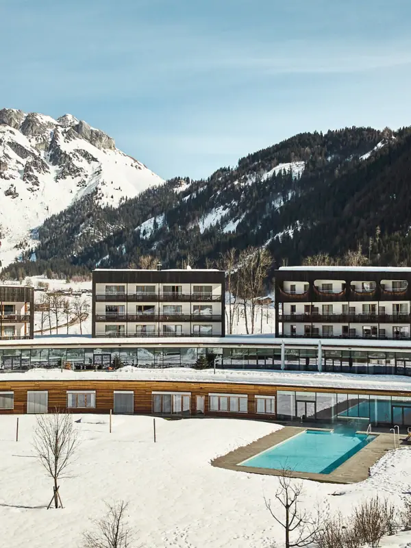 De Waterwereld in het aja Bergresort Werfenweng Het hotelgebouw met zijn buitenzwembad in de sneeuw, omringd door bergen.