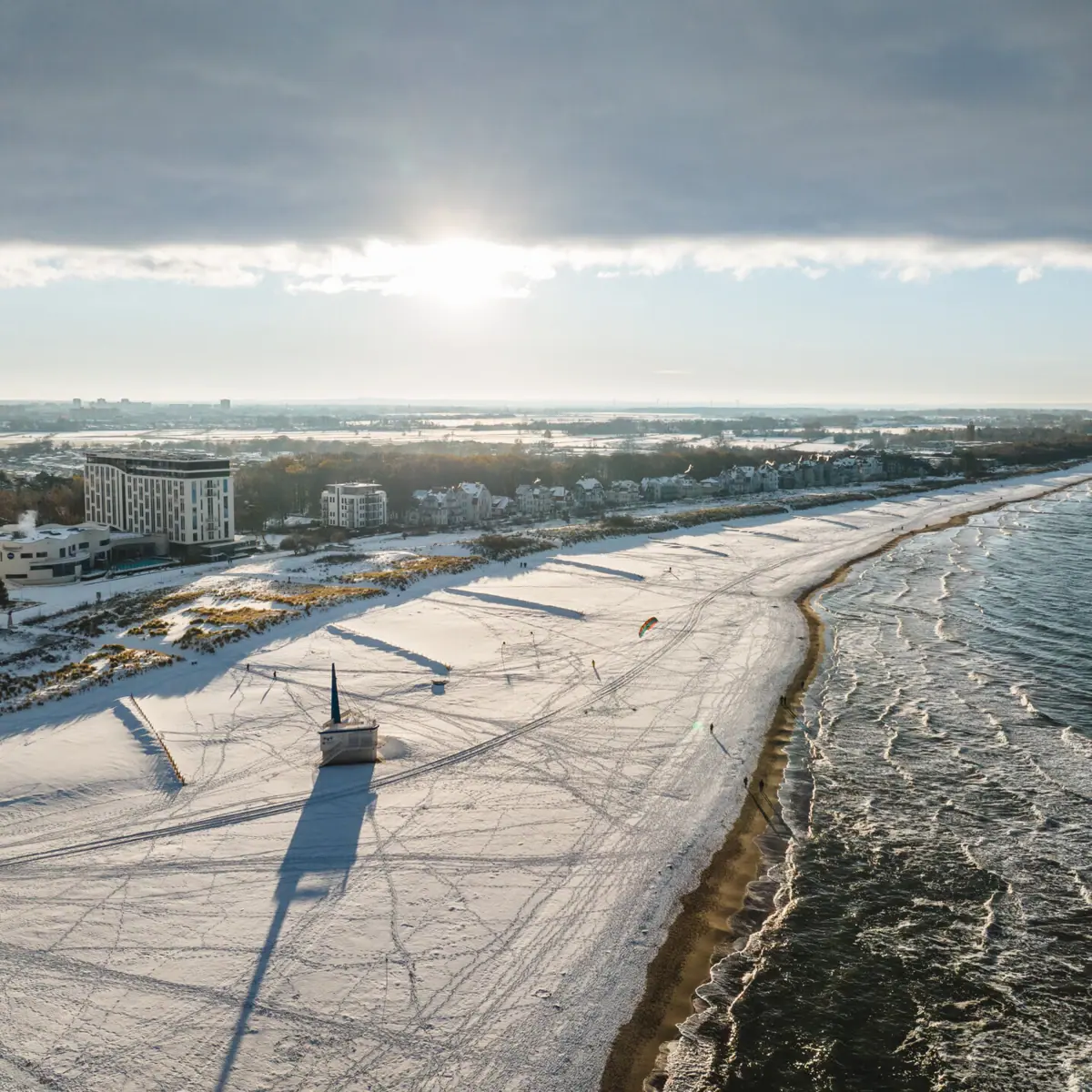 Oostzeestrand in de winter Een met sneeuw bedekt strand in Warnemünde in de winter, met gebouwen en water op de achtergrond.