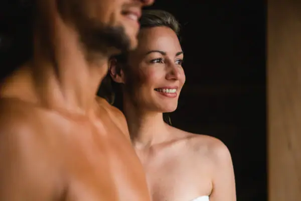 Een man en een vrouw staan lachend in een sauna.