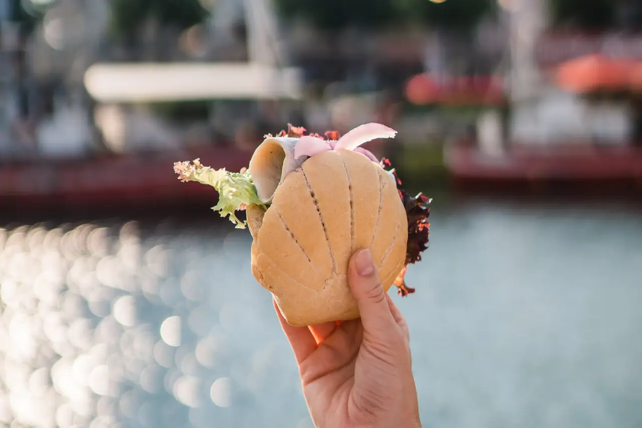 Eén hand houdt een visrol over glinsterend water.