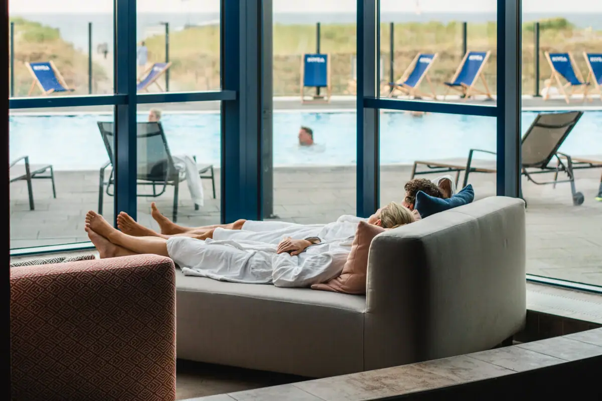 Ontspanningsruimte bij de aja Warnemünde Een vrouw ligt op een bank naast een zwembad.