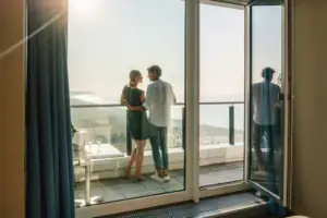 Suite bij de aja Warnemünde Een man en een vrouw staan op een balkon met uitzicht op een strand.